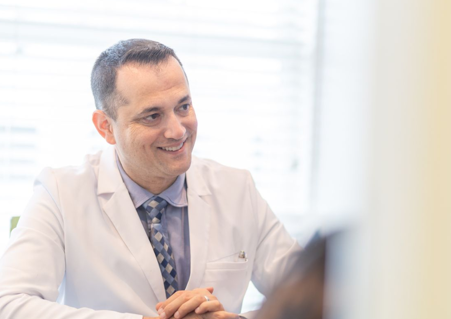 A dentist in a white coat sits at a desk.